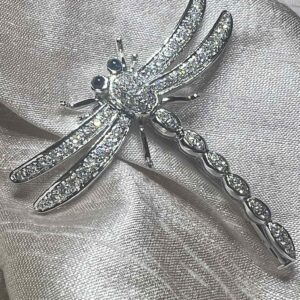 Elegant dragonfly brooch adorned with sparkling crystals on a soft fabric background.