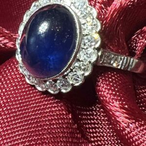 Elegant ring with a blue gemstone surrounded by small diamonds on a red fabric.